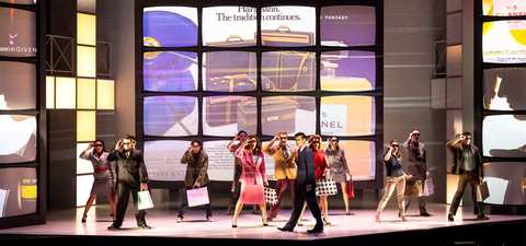 Sharpens the satire with bold production design and energetic music. Sharpens the satire with bold production design and energetic music.